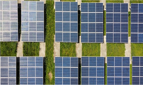 Aerial view of multiple rows of solar panels installed on grassy ground, arranged in a grid pattern.